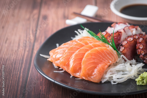 Salmon and Tako sashimi on black dish with chopsticks, Japanese food, wood background