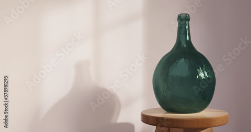 Empty green demijohn bottle in empty room, window shadow cast on wall. 3d rendering.