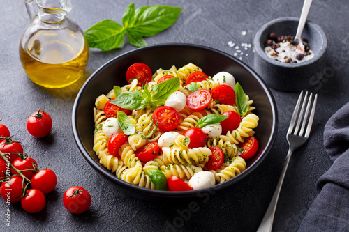 Pasta fusilli with mozzarella cheese, tomatoes and basil. Grey background. Close up.