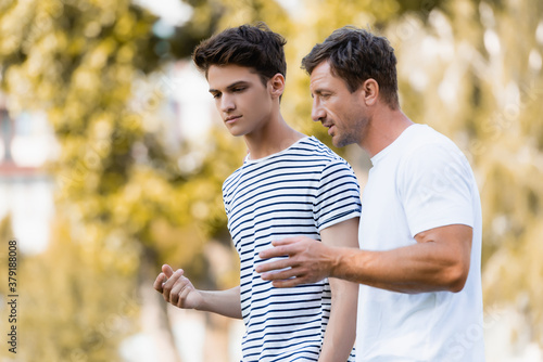 father gesturing and talking with teenager son in park