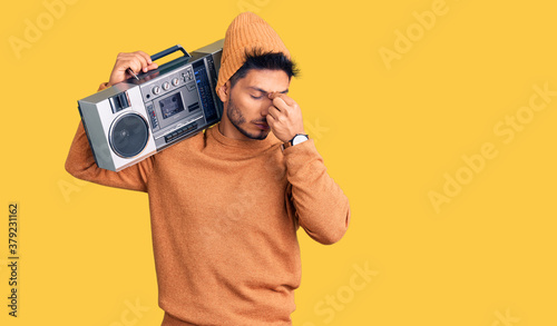 Handsome latin american young man holding boombox, listening to music tired rubbing nose and eyes feeling fatigue and headache. stress and frustration concept.