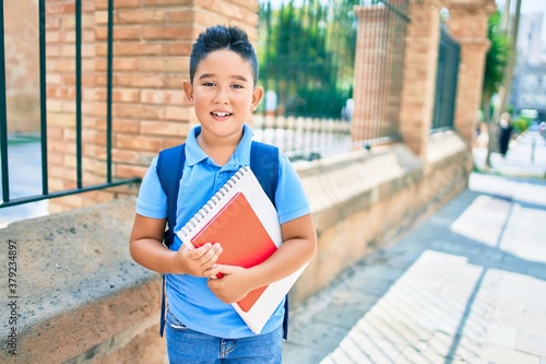 Adorable student boy smiling happy holding book at street of city.