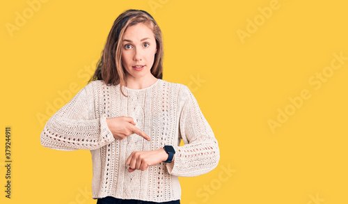 Young beautiful blonde woman wearing casual sweater in hurry pointing to watch time, impatience, upset and angry for deadline delay
