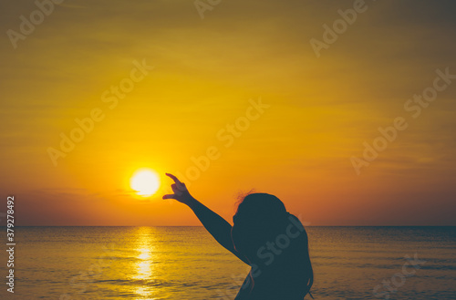 Silhouette woman walking on top of shore at sunset with sun in her hand.