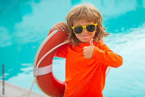 Little lifeguard show thumb up, ok. Summer kids holidays. Happy child playing with lifebuoy in the sea. Kids having fun on the beach.