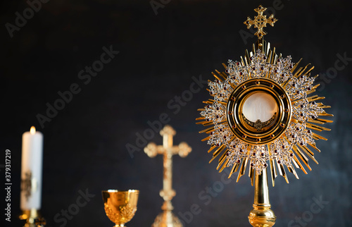 Catholic religion concept. Catholic symbols composition. The Cross, monstrance, Holy Bible and golden chalice on wooden altar. 