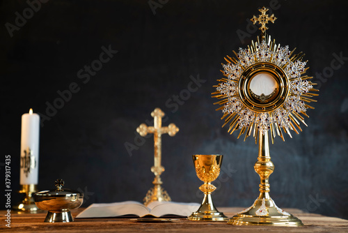 Catholic religion concept. Catholic symbols composition. The Cross, monstrance, Holy Bible and golden chalice on wooden altar. 