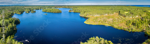 Breathtaking Aerial Panorama of Scandinavian green pine tree forest, dark blue lake with few small islands, Baltic Sea on horizon. Sunny day, Northern Scandinavia, high resolution photo
