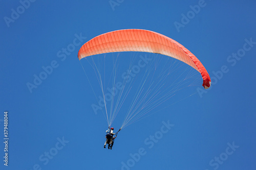 Blue Paraglider tandem instructor with a tourist flying into the sky with clouds on a sunny day