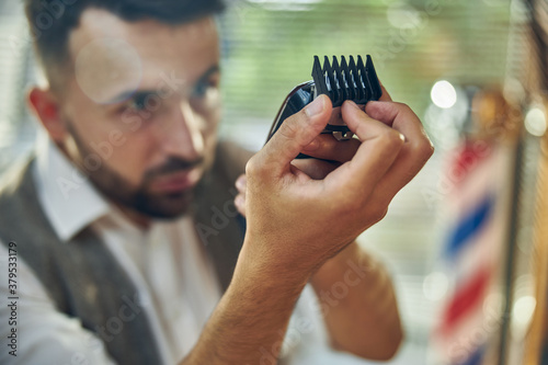 Professional barber looking attentively at an electric hair trimmer