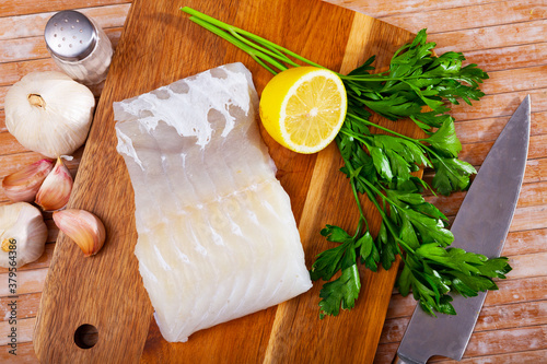 Piece of fresh rockling fillet on wooden surface with seasonings prepared for cooking