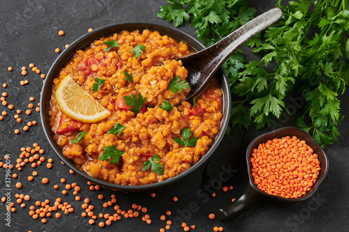 Red lentils dal in black bowl on dark slate table top. Lentils tomato dhal is indian cuisine dish with lemon and ciliantro. Indian food. Asian vegetarian meal