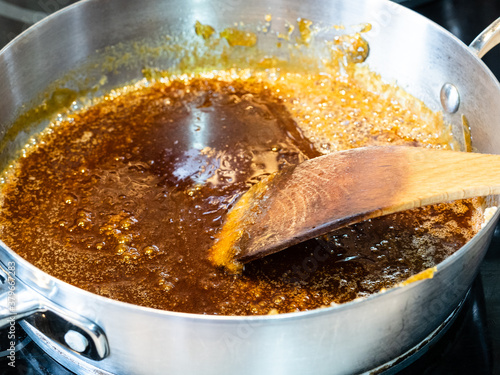 cooking salted butter caramel sauce at home kitchen - stirring melted mixture of sugar and butter with wooden culinary spatula in steel pan