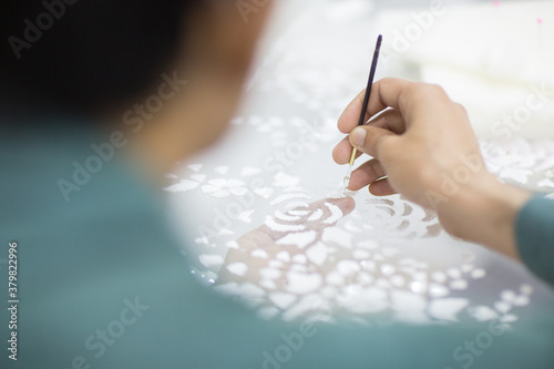 Closeup of dressmaker's hand embroidering beads pattern onto a white fabric. Haute couture dress making. 