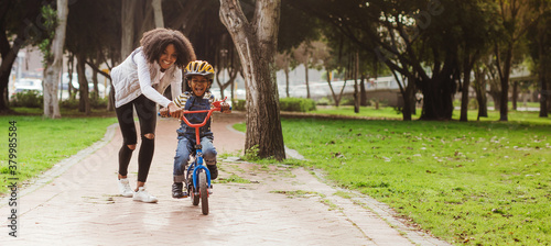 Little boy learning to ride bicycle at park with mother
