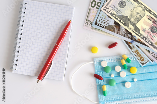 Medical mask, pills, money and notebook with pen on a white background.