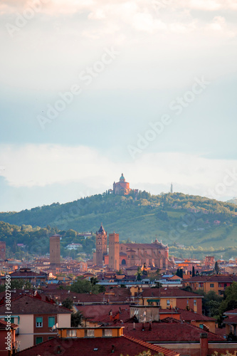 Aerial panoramic view of old Bologna city. It is saw Asinelli tower or torre, San Petronio church or basilica and San Luca church or basilica. Cloudy and sunset sky and bolognese hills in background