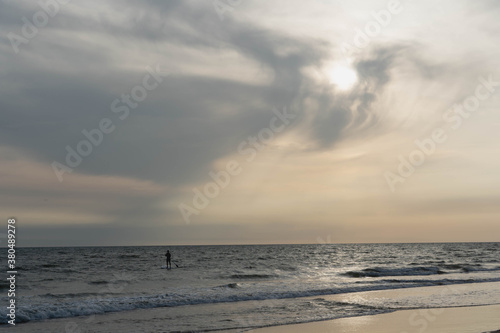 A surfer in with sunset on the beach in the background with a warm light.