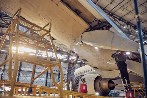 Men mechanics repairing of wing and engine of the aircraft in the hangar