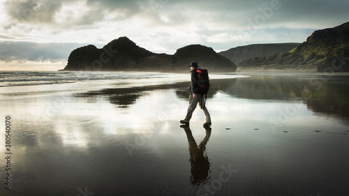 Walking on Bethells beach with reflection on the wet black sand, Waitakere, Auckland