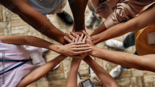 Top view of diverse young volunteers putting their hands on top of each other like a real team while standing in charitable organization office