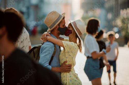 Young loving couple wearing protective face masks and kissing each other in the city. Love, lifestyle and virus spread prevention concept.