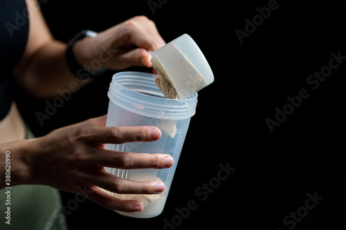 Close up of women with measuring scoop of whey protein and shaker bottle, preparing protein shake.