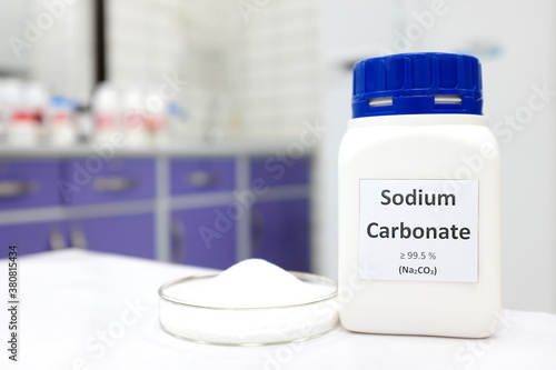 Selective focus of a bottle of sodium carbonate chemical compound or soda ash beside a petri dish with solid crystalline powder substance. White Chemistry laboratory background with copy space.