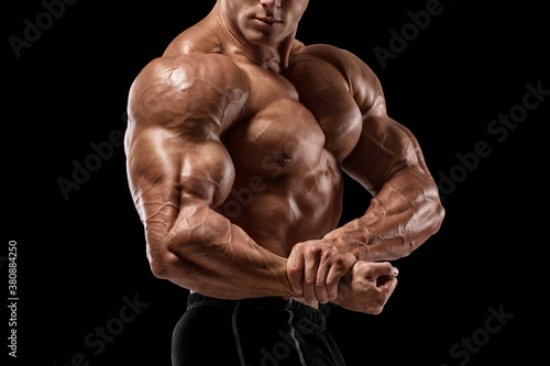 Muscular man showing muscles and biceps isolated on black background. Bodybuilder male naked torso abs