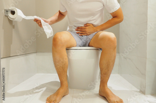 Man sitting in the toilet using his hand pulling toilet paper feeling painful after eating unhygienic food Stomach ache and human healthcare concept