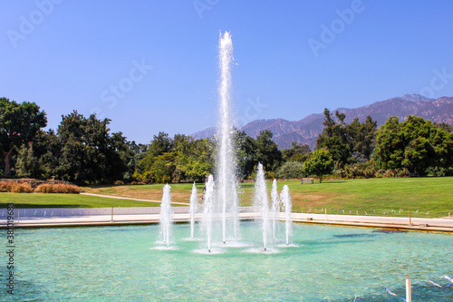 a gorgeous summer landscape at the LA Arboretum with a water fountain, lush green trees, plants and grass, mountains and blue sky in Arcadia California USA