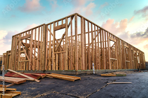 New construction house framing of residential home in California with beautiful blue and pink sunset sky filled with clouds and lumber laying around the construction site property
