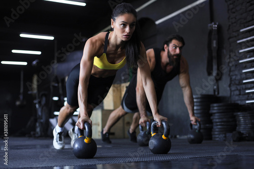Sporty indian man and woman doing push-up in a gym.