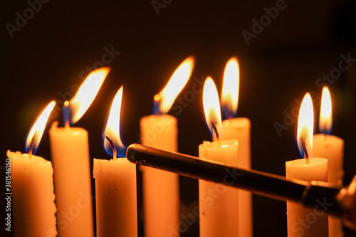 Close up photo of a candlelight being ignited using a portable fire igniter, close up of burning candles in the dark.