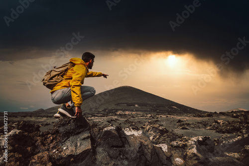 Successful hiker hiking a mountain pointing to the sunset. Wild man with backpack climbing a rock over the storm. Success, wanderlust and sport concept.