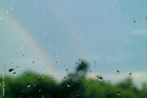 Closeup rain drops on window glass with blurry twin rainbows in background