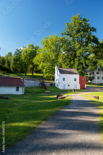 Sheep graze in an idyllic colonial village scene at Hopewell Furnace National Historic Site. White stone cottage and ethereal summer scene in a Pennsylvania landsape.