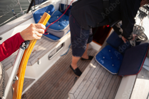 Senior woman steering sailing boat while man is stowing the ropes. Focus on steering hand.
