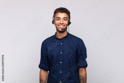 young telemarketer man smiling happily with a hand on hip and confident, positive, proud and friendly attitude