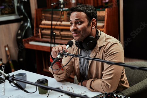 Portrait of young male radio host looking focused while speaking in microphone, moderating a live show