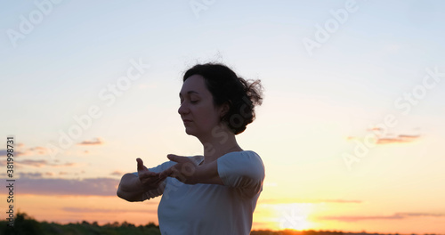 Female practicing qigong in summer fields with beautiful sunset on background 