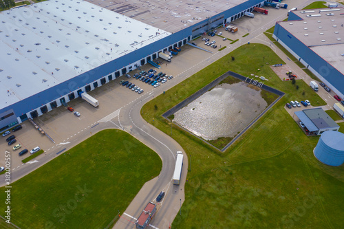 Aerial Top View of Industrial Storage Building Area with Solar Panels on the Roof and Many Trucks Unloading Merchandise.