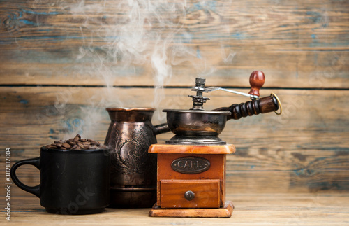 The process of making coffee. Smoking coffee beans in coffee cup and coffee grinder on the table are items for making coffee. Place for text. Black background.