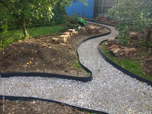 Landscape of garden design project building constructing a winding path with antique recycled house bricks, shape cut in grass ground and hard core base, edging laid before sand stone laying in Autumn