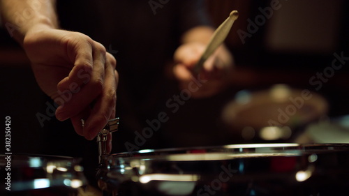 Unrecognizable musician tuning drum kit in studio. Drummer hitting drum in hall.