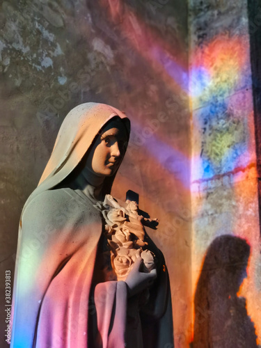 Saint therese of lisieux statue, with magnificent stained glass reflections, in a french catholic church.