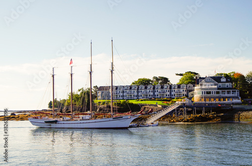 Luxurious and elegant Victorian architecture New England wooden cottage resort or hotel in Bar Harbor, Maine with beautiful sailing yacht or windjammer on sunny morning