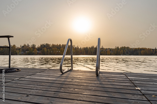 Wooden pier with stairs on lake with autumn sunset