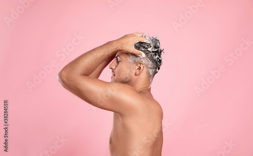 Handsome man washing hair on pink background
