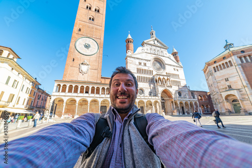 happy tourist visiting the city of Cremona taking selfie in the middle of main square of Cremona with Cathedral, baptistery and Torrazzo bell tower . 